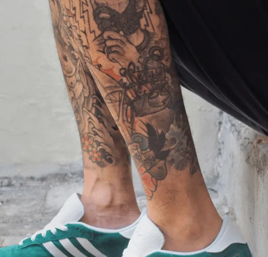 Full black-and-grey leg sleeve tattoo covering the calf and ankle