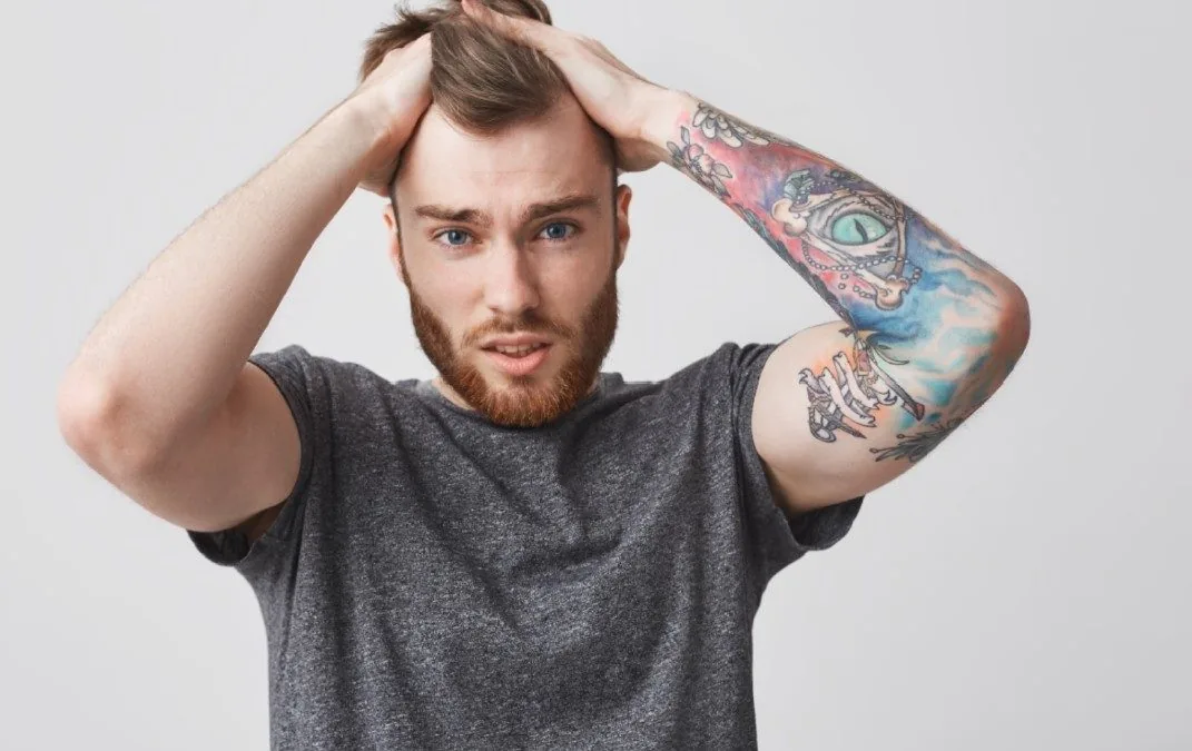 Man with a full arm sleeve tattoo, hands raised to his head